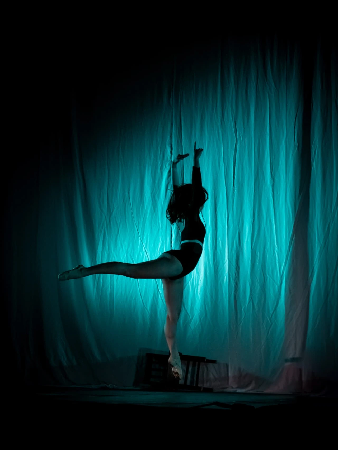 Bailarina de DANZAR en arabesque a contraluz sobre fondo turquesa