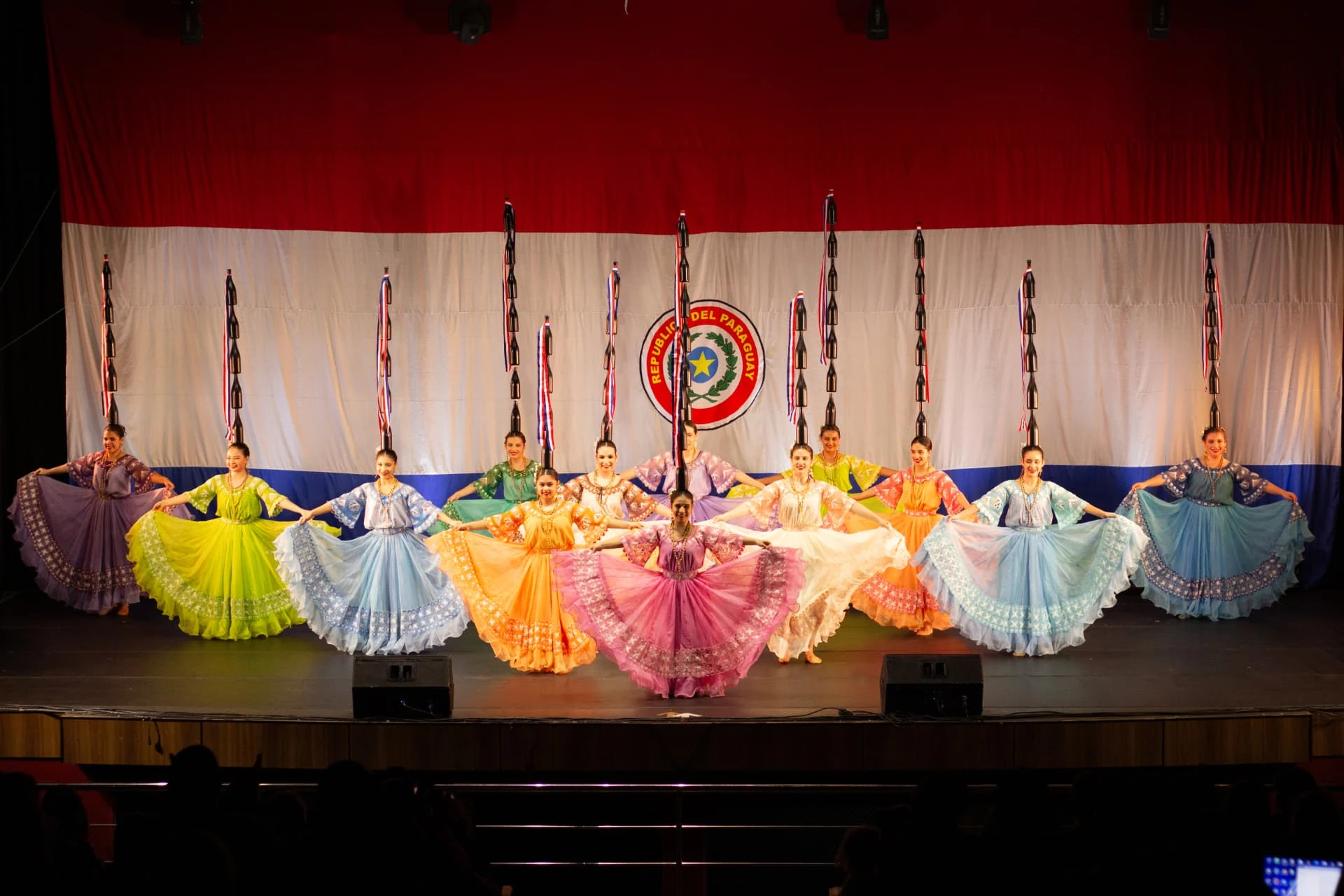 Elenco de danza paraguaya con cántaros frente a la bandera nacional